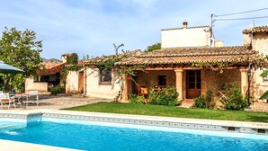 A swimming pool with a tiled edge, a patio with chairs, and a building with a tiled roof and stucco walls. - Villa Can Mart By SunVillas Mallorca (Pollença)