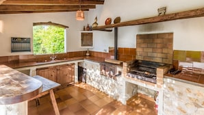 A rustic kitchen with a brick oven, wooden beams, and a window overlooking greenery. - Villa Can Mart By SunVillas Mallorca (Pollença)