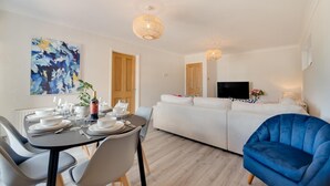 Un salon moderne comprenant un coin repas, des canapés blancs, un fauteuil bleu et un téléviseur à écran plat.