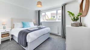 Une chambre d’hôtel moderne, équipée d’un lit, de tables de chevet, d’un radiateur, d’une fenêtre avec des rideaux et d’une plante en pot.