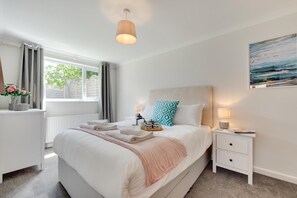 A neatly arranged bedroom with a bed, bedside tables, a window with curtains, a radiator, and a wall-mounted painting.