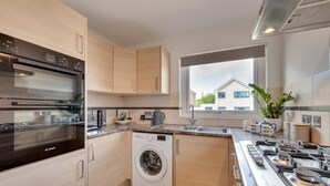 Une cuisine moderne équipée d’un four Bosch, d’un lave-linge et d’une grande fenêtre offrant une vue sur une maison à l’extérieur.
