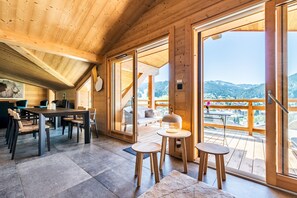 Una cabaña de madera con comedor, un balcón con vistas a las montañas y un dormitorio acogedor con cama y mesita de noche.