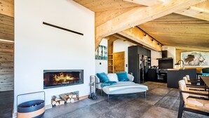 Un interior modern amb una llar de foc, un sofà amb coixins, una zona de menjador amb cadires i una cuina.
