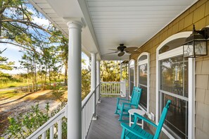 Une véranda couverte avec deux chaises turquoise, un ventilateur de plafond et une vue sur une route et des arbres.