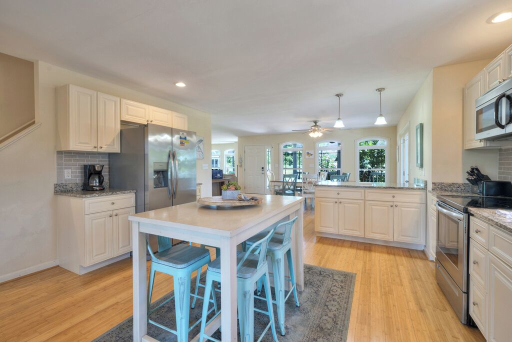 A spacious kitchen with white cabinetry, a central island with bar stools, stainless steel appliances, and pendant lighting.