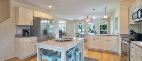 A spacious kitchen with white cabinetry, a central island with bar stools, stainless steel appliances, and pendant lighting.