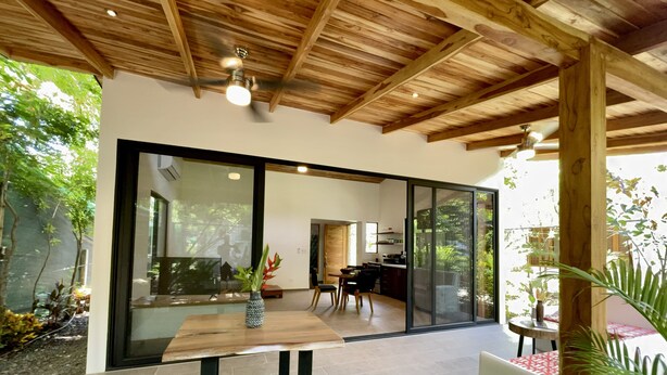 Una cucina moderna con un'isola grande, un'area pranzo con tavolo in legno e una porta scorrevole in vetro che dà su un giardino.