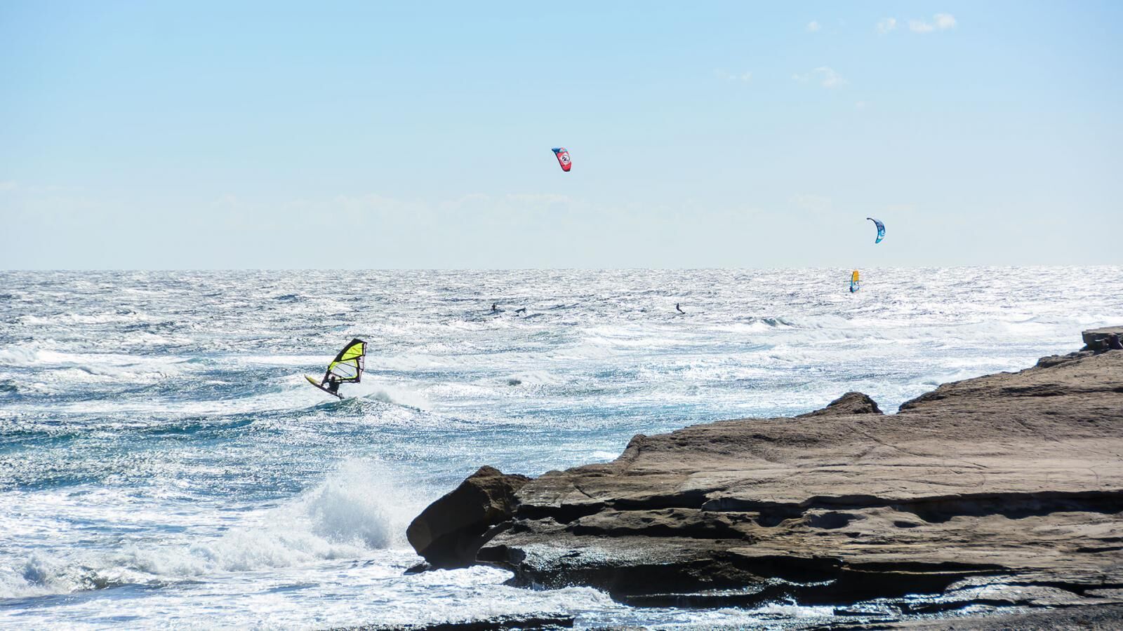 A coastal scene with a person windsurfing and kitesurfing.