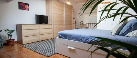 A bedroom with a bed, a dresser, a TV, and a potted plant.