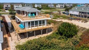 A beachfront house with a wooden deck, a covered outdoor area, and a view of the beach.