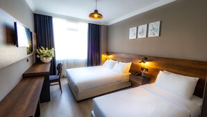 Une chambre d’hôtel avec deux lits, un bureau, une chaise, une télévision et des œuvres d’art accrochées au mur.