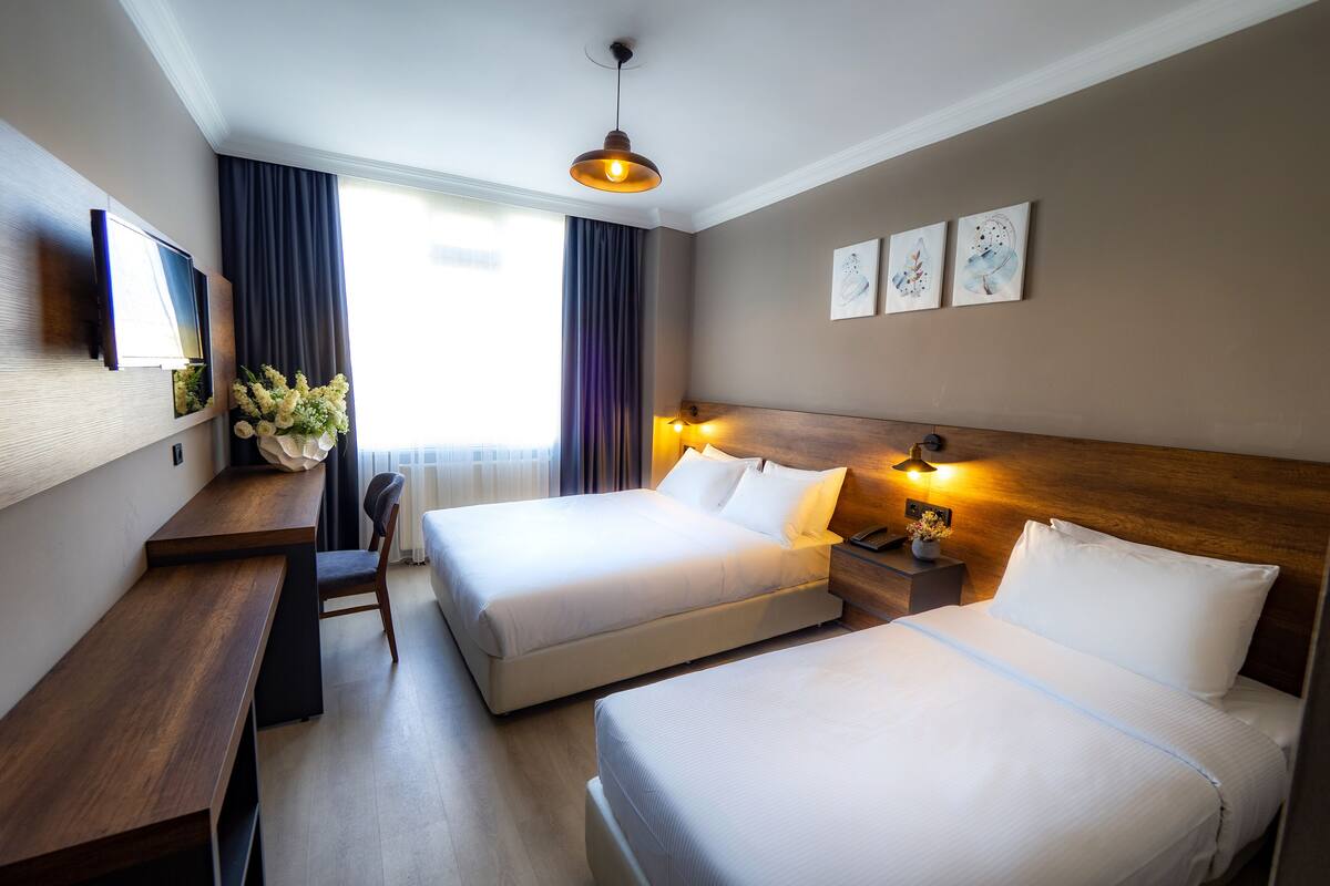 A hotel room with two beds, a desk, a chair, a TV, and artwork on the wall.