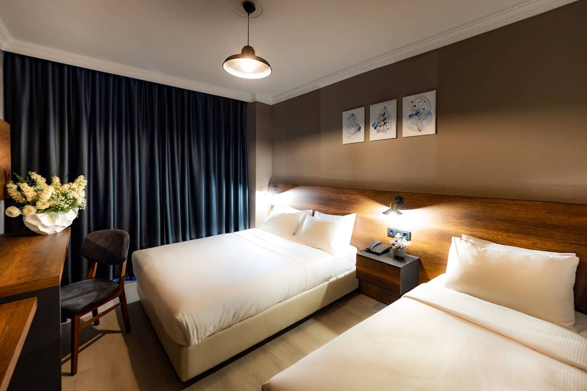 A hotel room with two beds, a desk with a chair, a vase of flowers, a wooden headboard, and artwork on the wall.