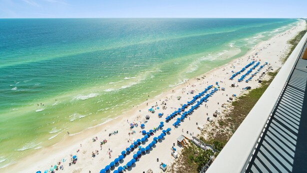 Ein Strand mit blauen Sonnenschirmen und freiem Blick auf das Meer.