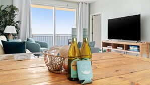 Ein Wohnzimmer mit einem Holztisch, zwei Weinflaschen, einem Korb voller Dekoration, einer Couch und einem Fernseher auf einem Holzständer.