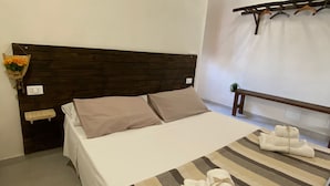 Un lit bien fait, avec une couvre-lit à rayures, une tête de lit en bois et une table de chevet sur laquelle se trouve un panier de fleurs.