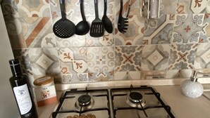 Une cuisine équipée d’une cuisinière à gaz, d’un porte-ustensiles, d’une bouteille d’huile d’olive et d’un bocal de thé.
