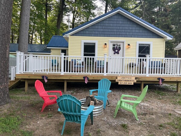 A yellow vacation rental with a white deck, blue and red Adirondack chairs, and a sign indicating the rental name and contact number. - If you love water & outdoor activities this is the place for you!! (Indian River)
