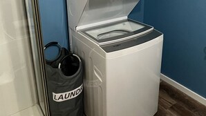 A compact, white laundry machine with a control panel, placed against a blue wall.