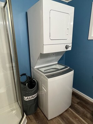 A compact, white laundry machine with a control panel, placed against a blue wall.