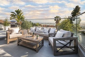 A rooftop terrace with a sofa set, a wooden coffee table, and a grill.