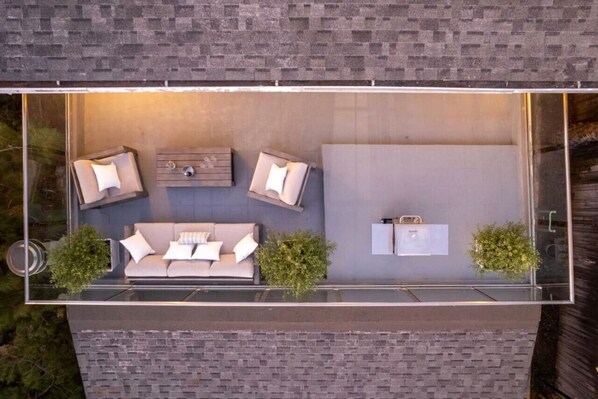 A modern outdoor living space with a glass enclosure, a sofa set, a coffee table, and a small kitchen area.