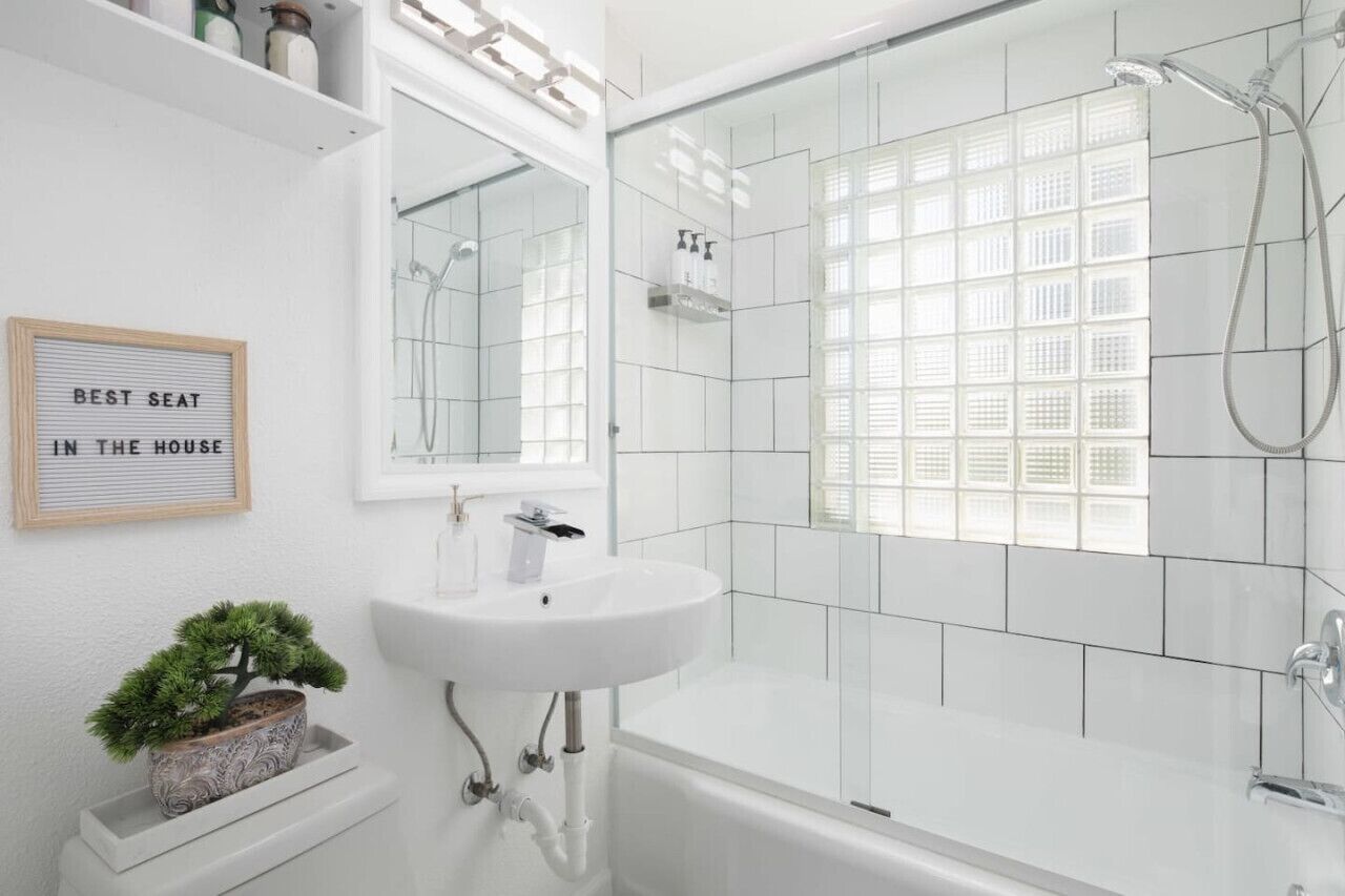 Un baño moderno con un lavamanos blanco, una ducha con cerramiento de vidrio y un ventanal de diseño de cuadrícula.