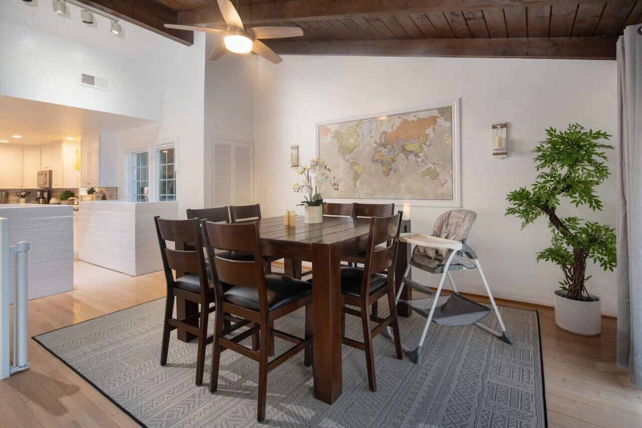 A dining area with a wooden table and chairs, a map on the wall, and a potted plant.