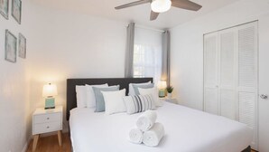 A neatly made bed with white linens and rolled towels, a dark headboard, bedside lamps, and a ceiling fan.