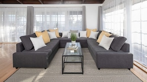 A modern living room with a sectional sofa, a glass coffee table, and sheer curtains.