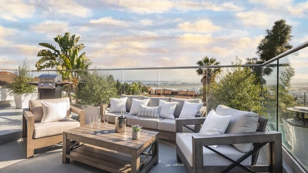 A rooftop terrace with a sofa set, a wooden coffee table, and a grill.