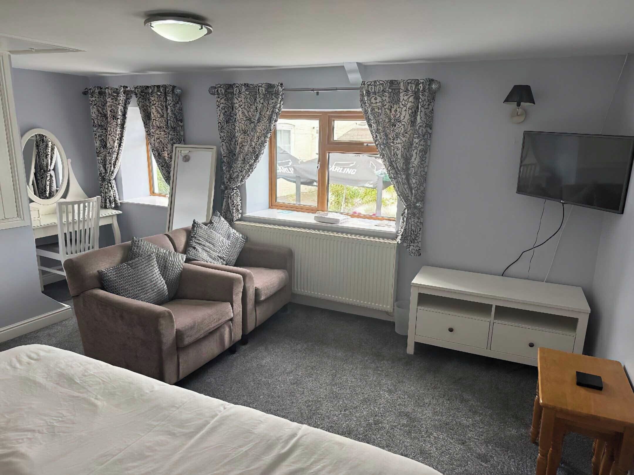 A bedroom with a bed, a chair, a desk, a television, and a window with curtains.