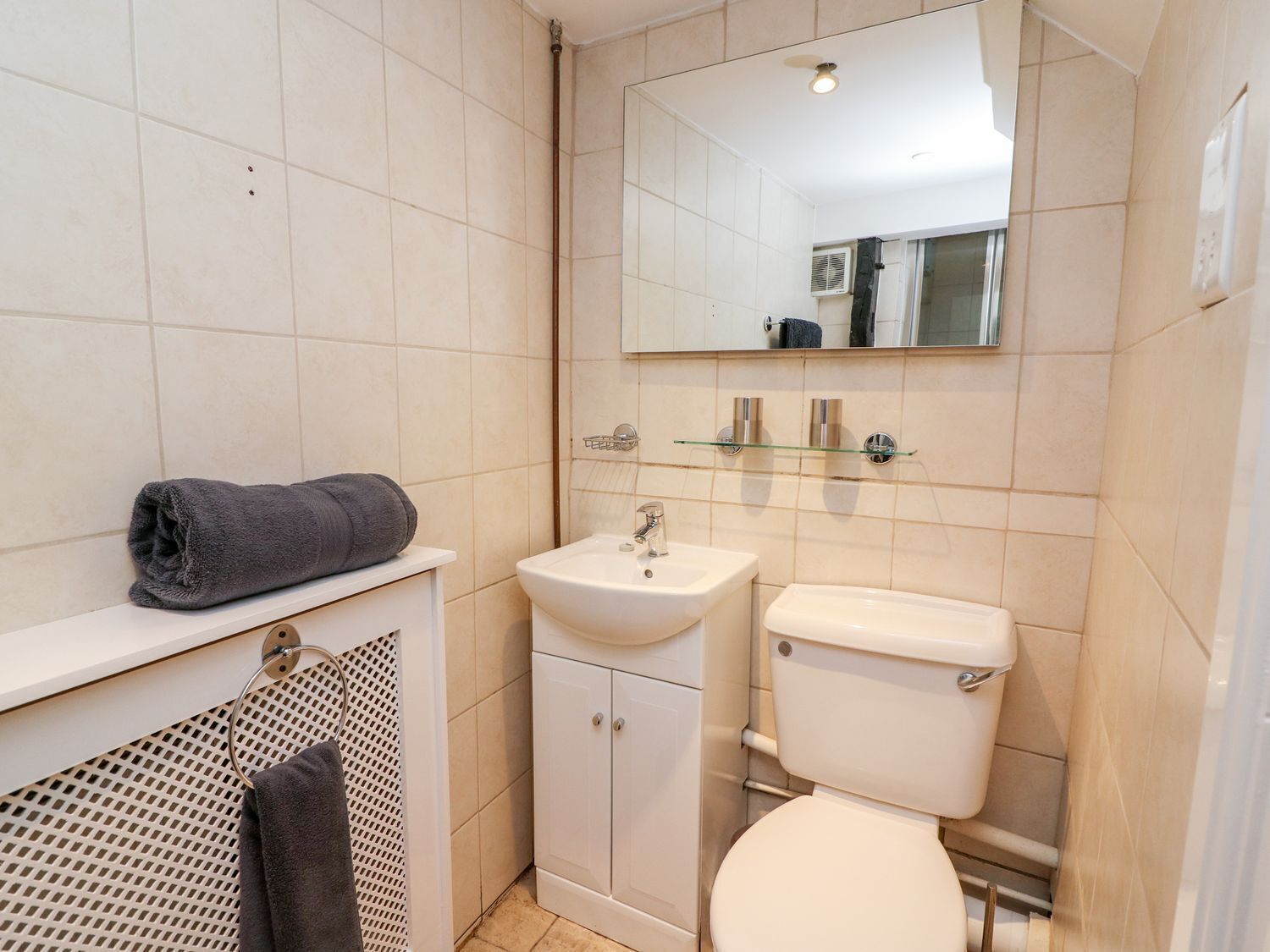 A small, clean bathroom with a toilet, sink, and mirror.
