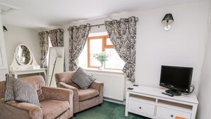 Une chambre meublée avec deux fauteuils, un téléviseur, une armoire blanche et une fenêtre agrémentée de rideaux à motifs.