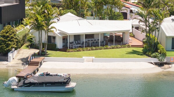 A modern house with a covered patio, a boat dock, and a well-maintained lawn. - Wesley Court No. 21 Noosa Sound (Noosa Heads)