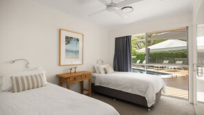 A hotel room with two beds, a wooden nightstand, a framed picture, a ceiling fan, and a view of an outdoor pool area. - Wesley Court No. 21 Noosa Sound (Noosa Heads)