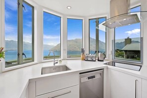 A modern kitchen with large windows offering a view of mountains and a lake.