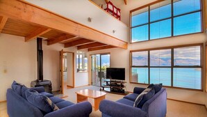 A spacious living room with a high ceiling, large windows, and a fireplace. - Ruby's Fernhill Vista (Queenstown)