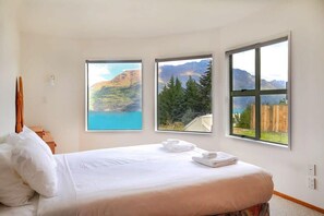 Une chambre à coucher comprenant un lit, une table de chevet et trois fenêtres donnant sur les montagnes.