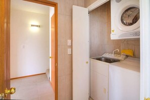 Une buanderie équipée d’un lave-linge, d’un évier et d’une porte donnant sur une autre pièce.