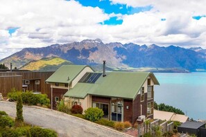 Une maison moderne dotée d’un toit végétalisé, de grandes fenêtres et offrant une vue sur les montagnes et un lac.