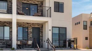 Un immeuble à deux étages au design moderne, doté d’un balcon à l’étage supérieur, d’un escalier menant à l’entrée et d’un parking à l’avant.