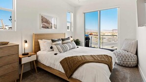 Une chambre à coucher avec un grand lit, une table de chevet, une commode en bois et une fenêtre donnant sur un paysage désertique.