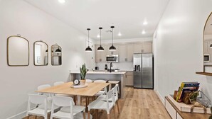 Une cuisine moderne avec des armoires blanches, des appareils en acier inoxydable et des luminaires suspendus.