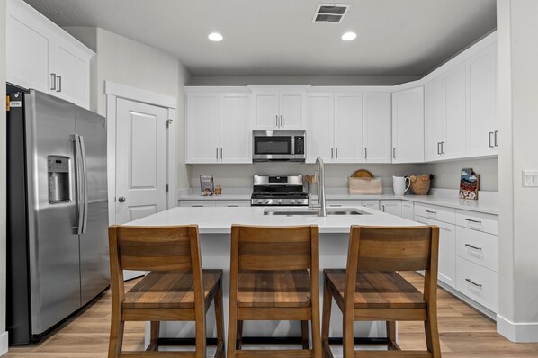 A modern kitchen with white cabinets, stainless steel appliances, and wooden chairs.