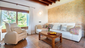 Una sala de estar con un sofá blanco, una mesa de centro de madera con frutas, y una pared de piedra.