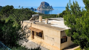 Un edificio con techo plano, paneles solares y vista al mar y una isla rocosa.