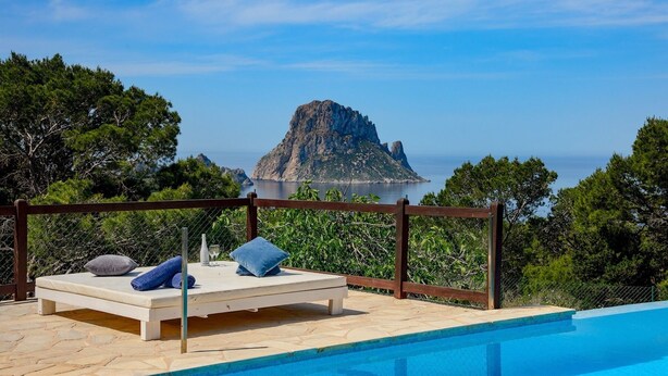 Un área de descanso junto a la piscina con vistas a una isla rocosa y al mar.