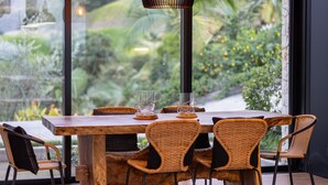 A wooden dining table with wicker chairs, a glass candle holder, and a hanging light fixture.